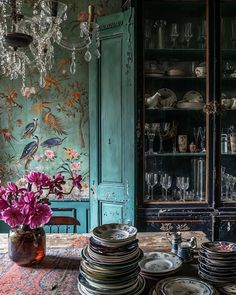 a table topped with lots of plates next to a vase filled with flowers and wine glasses