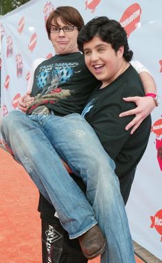 two young men sitting on top of each other in front of a red carpeted area