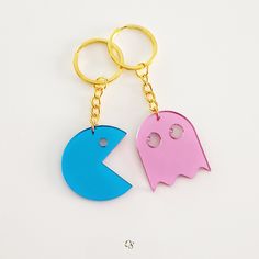 two key chains with pacman and ghost faces on them, one is pink and the other is blue