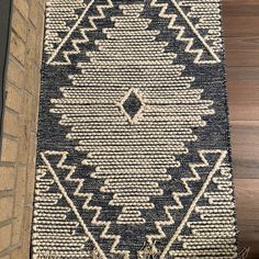 a black and white rug sitting on top of a wooden floor next to a brick wall