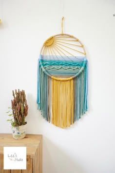 a wall hanging made out of macrame and yarn with a plant next to it