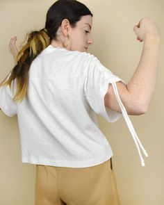 a woman in white shirt and tan pants holding a wii controller up to her chest