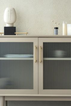 a white cabinet with glass doors and some dishes on it's top shelf in front of a wall