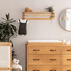 a baby's room with a dresser, mirror and hanging clothes on the wall