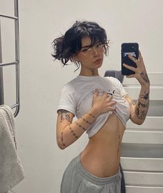 a woman with tattoos taking a selfie in the mirror while wearing shorts and a t - shirt