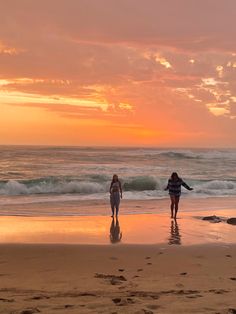 two women walking on the beach at sunset