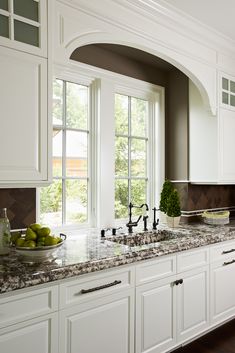 a kitchen with marble counter tops and white cabinets, along with an arched window over the sink