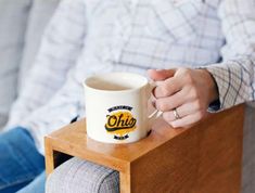 a person sitting on a couch holding a coffee mug with the word ohh written on it