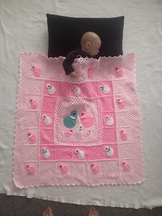 a crocheted pink blanket with teddy bears on it and a black pillow next to it