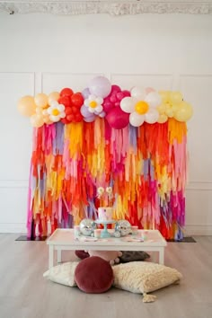 a table with cake and balloons on it in front of a colorful wall hanging from the ceiling