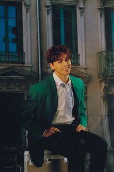 a man in a green jacket and white shirt is sitting on a ledge outside an apartment building