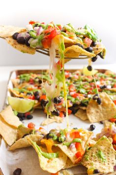 a tortilla chip being dipped with guacamole and black olives