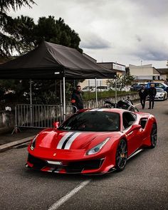 a red sports car parked on the side of the road with people walking by it