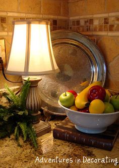 a bowl of fruit on a table next to a lamp