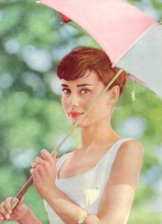 a woman holding an umbrella while standing in front of some trees with her hand on the handle