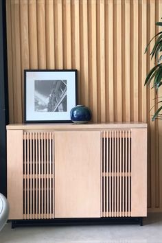 a wooden cabinet with two doors and a black vase on top next to a plant