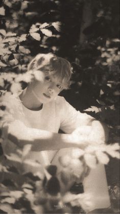 a black and white photo of a young boy sitting on a bench surrounded by leaves