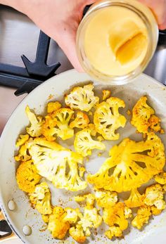 a person is pouring something into a pan with some cauliflower florets