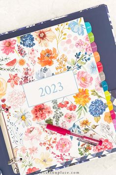 a planner with flowers on it, next to a pen and marker board that says 2013