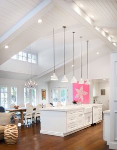 a large open concept kitchen and dining room with white cabinets, wood flooring and high vaulted ceilings