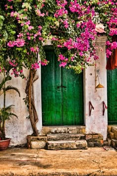 an old building with green doors and pink flowers growing on the outside, along with steps leading up to it