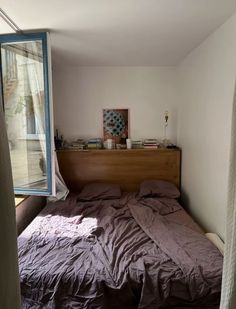 an unmade bed sitting next to a window in a bedroom