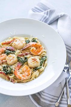 a white bowl filled with pasta and shrimp on top of a table next to silverware