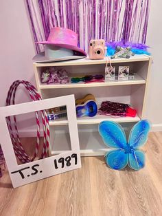 a shelf filled with hats and other items on top of a hard wood floor next to a pink curtain