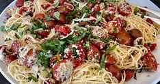 a white plate topped with pasta covered in tomatoes and parmesan sprinkles