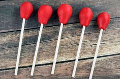 four red heart shaped lollipops sitting on top of a wooden table next to each other