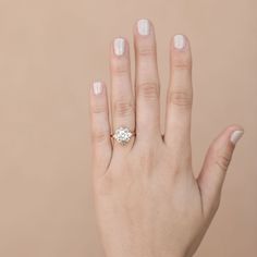 a woman's hand with a diamond ring on her left hand, against a beige background