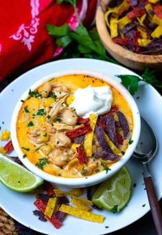 a white plate topped with a bowl of soup next to limes and tortilla chips