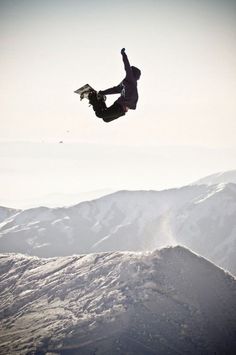 a man flying through the air while riding a snowboard on top of a mountain