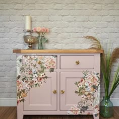 a pink dresser with flowers painted on the front and drawers, next to two vases