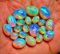 a person is holding several opal stones in their hand, all different colors and shapes