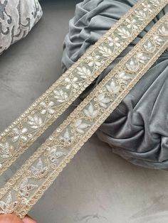 two silver and gold lace trims sitting on top of a gray pillow next to pillows