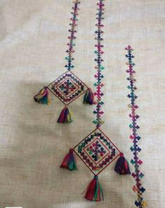 two tasselled beads are hanging from the side of a piece of cloth with multicolored fringes