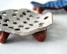 two small ceramic objects sitting on top of a white tableclothed surface, one with holes in it and the other without