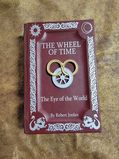 the wheel of time book with two gold rings on it sitting on a brown blanket