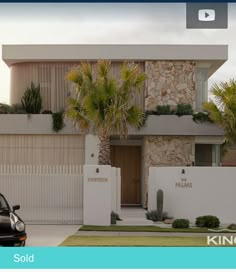 a car parked in front of a house with palm trees on the side and a white fence