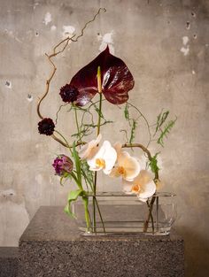 a vase filled with flowers on top of a stone block next to a concrete wall