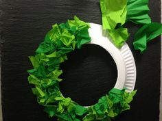 a paper plate wreath made with green tissue paper on a black surface, next to a piece of construction paper