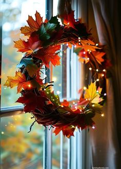 a wreath is hanging on the window sill with autumn leaves around it and lights in the background