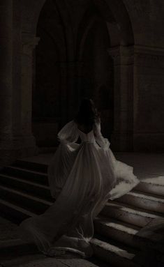 a woman in a long white dress is sitting on some steps and looking at something