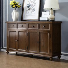 a wooden sideboard with two lamps on top and pictures above it in front of a window