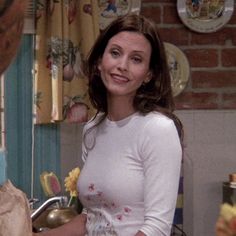 a woman standing in a kitchen next to a sink and counter with dishes on it