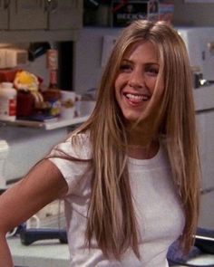 a woman with long blonde hair standing in front of a kitchen counter smiling at the camera