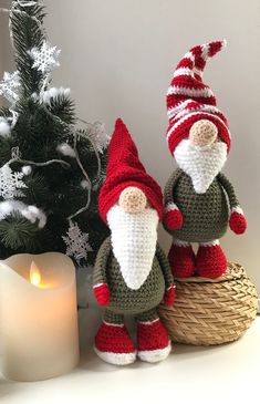 two crocheted gnomes sitting next to a christmas tree with a lit candle