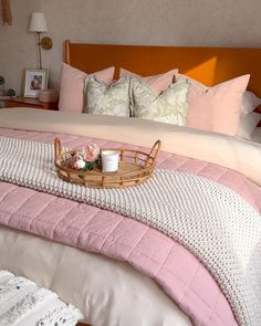 a bed with pink and white comforters, pillows and a basket on it