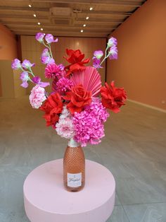 a vase filled with pink and red flowers on top of a round table in an empty room